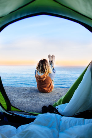 A view from a tent of a beautiful young woman relaxing on the sandy beachの写真素材