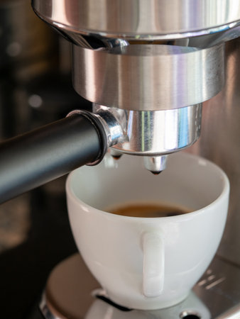 A close-up shot of a coffee being poured in a white ceramic cup from a coffee machineの写真素材