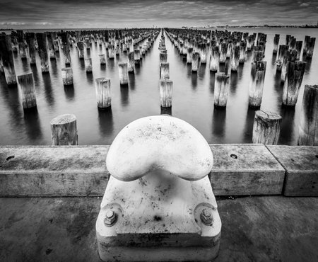 A grayscale shot of an old pier and a bollard by the seaの写真素材