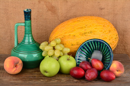 A green decanter, peaches, a melon, green apples, and red plums in a rustic compositionの写真素材