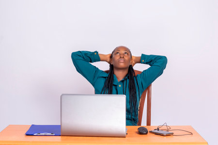 The young African woman sitting at the desk, leaning back on the chair and looking up.の写真素材