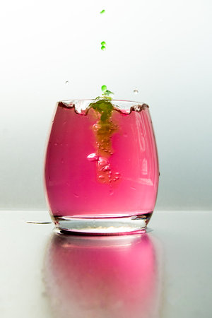A vertical shot of a glass of pink water with splashes and green paintの写真素材