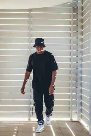A vertical shot of a young black man from Spain in street-style black clothing and bright shoes