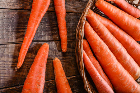 A wicker basket full of fresh carrots on a wooden tableの写真素材