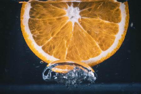 A closeup shot of an orange slice splashing in waterの写真素材