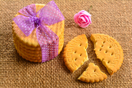 A top view of a small cookie gift with a violet ribbon and a cracked cookie on a straw surface