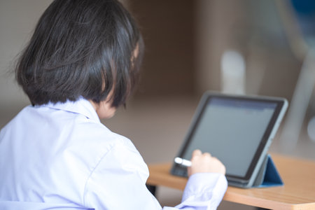 A Southeast Asian school girl in a uniform with short black hair drawing on a tablet with a pen
