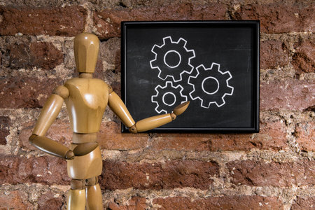 A wooden mannequin showing business gears on chalkboard, blackboard over a brick wall backgroundの写真素材