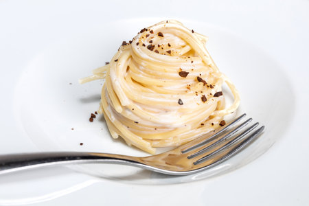 A closeup shot of a delisous vegan pasta dish with fork on a white plateの写真素材