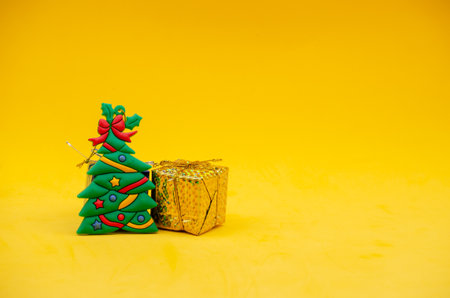 A decorative Christmas tree figure next to a gift isolated on a yellow backgroundの写真素材
