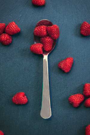 A vertical shot of a spoon with raspberries on slate backgroundの写真素材
