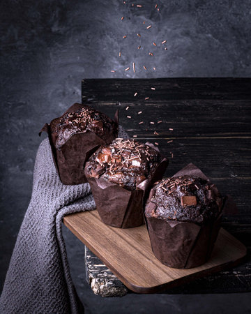 A vertical closeup shot of three delicious chocolate muffins on a dark gray backgroundの写真素材