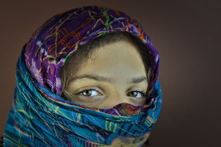 A portrait of a caucasian girl covering the head with a scarf on a dark backgroundの写真素材