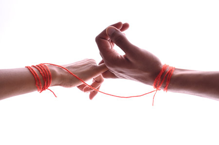A male and female hands wrapped in red thread isolated on white, concept of desire and loveの写真素材