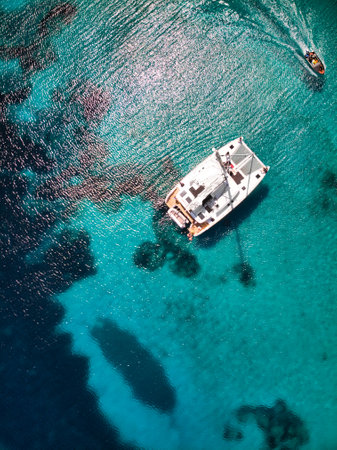 A bird's eye view of a white boat, swimming in the blue, shining sea under the sunlightの写真素材