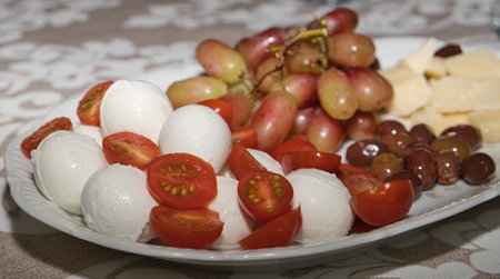 A typical Mediterranean starter with buffalo mozzarella, tomato, olives, parmesan cheese, and grapesの写真素材