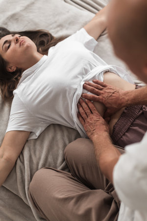 A middle-aged Caucasian bald masseur and a woman doing Japanese belly massage exercises on a mat at homeの写真素材