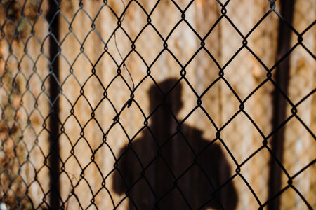 A view of the shadow of a male behind the net fence in Bayreuthの写真素材