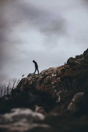 A vertical shot of male standing on rocks in Sweden mountains in background of rainy skyの写真素材