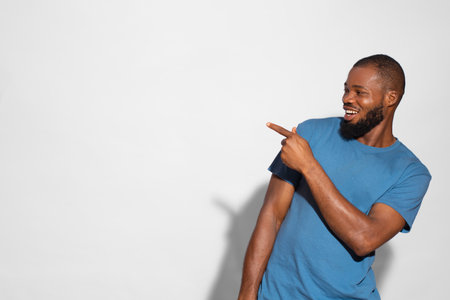 A black man with a blue t-shirt smiling and showing something on a white background.の写真素材