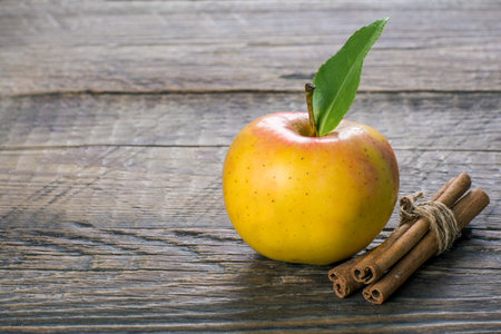 A Closeup shot of apples and cinnamon sticks on a wooden surfaceの写真素材