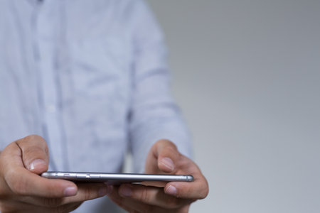 A businessman holding a smartphone against a gray backgroundの写真素材