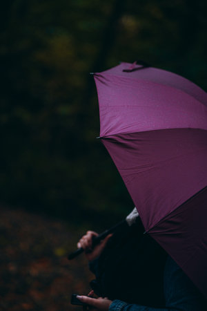 A vertical shot of a person holding a dark purple umbrellaの写真素材
