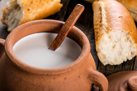 A closeup of halved crunchy french baguette and the milk crock jug on the wooden surfaceの写真素材