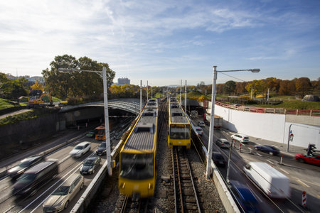 The trains moving on the railroad bridge over the busy traffic road against a cloudy skyの写真素材