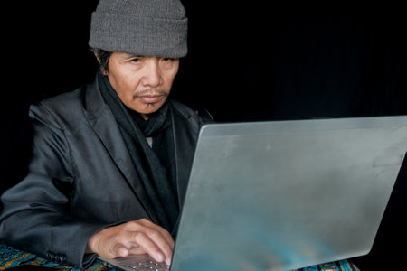 An East-Asian businessman working on a laptop against a black backgroundの写真素材