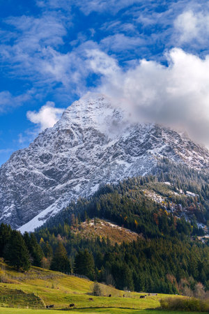 A vertical shot of a snowy mountain enveloped in clouds on a sunny dayの写真素材