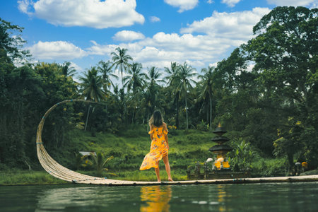 A young adult woman wearing a long yellow dress on a dock on a lake in Ubud, Bali, Indonesiaの写真素材