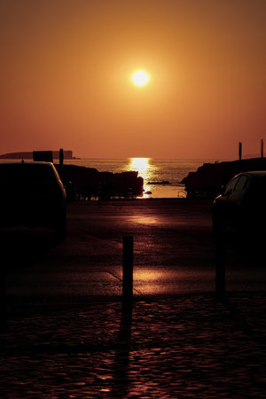 A vertical shot of a beautiful seascape with cars parked at the shore at scenic sunsetの写真素材