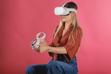 A blonde lady from Belgium playing a virtual reality game isolated on a pink backgroundの写真素材