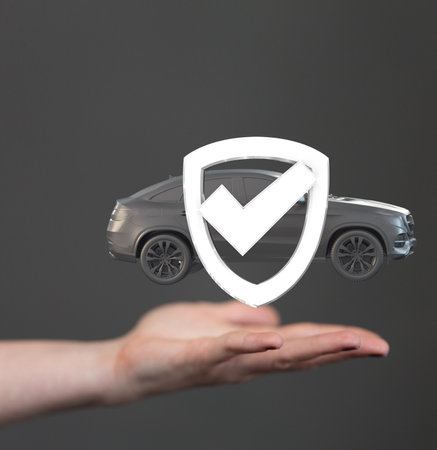 A 3D rendered car and shield check mark icon over a person's hand isolated on gray backgroundの写真素材