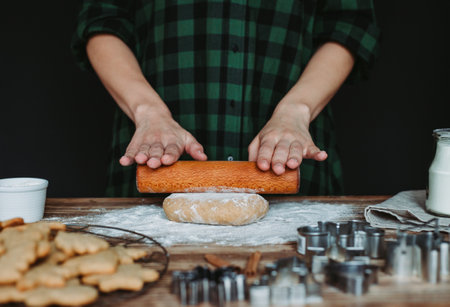 A female baker's hands cutting gingerbread cookies for Christmas on a rustic wooden boardの写真素材