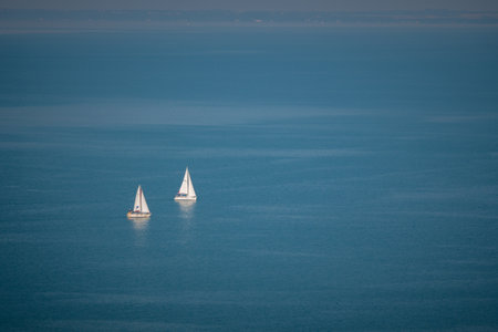 A tranquil scenery of two sailboats in the endless azure oceanの写真素材