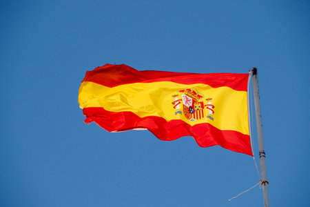 The flag of Spain hung on a pole in the background of a blue sky.の写真素材