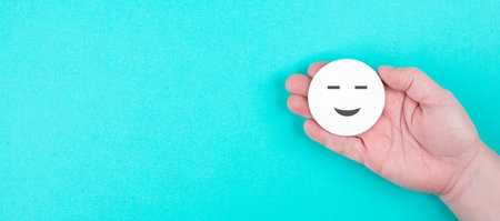 Holding a smiling face in the hand, blue colored background, copy space, rating, positive feedback,...