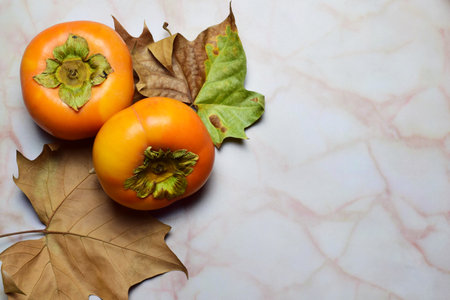 A zenith view of persimmon fruits and autumn natural leaves on a marble background with a copy spaceの写真素材