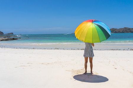 A woman wearing a light dress and holding an umbrella at a beach on a sunny day in Kuta, Lombokの写真素材