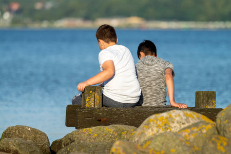 Two kids sitting on a wooden pier by the seaの写真素材