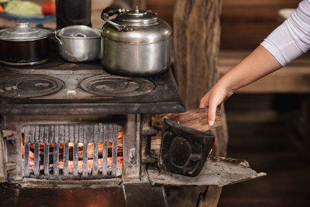 A woman putting firewood into an old metal oven with kitchen pots on the top in Tilaran, Guanacaste,...