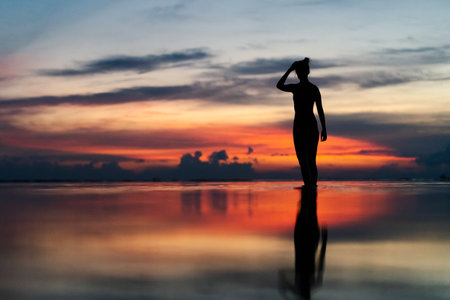A silhouette of a woman at the beach surrounded by the sea with long exposure during the sunset in Gili Air, Indonesiaの写真素材
