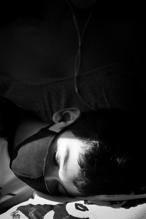 A grayscale shot of a sleeping boy with a maskの写真素材