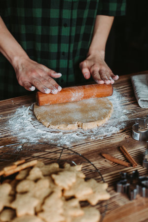 A female baker's hands cutting ginger cookies for Christmas on a rustic wooden boardの写真素材
