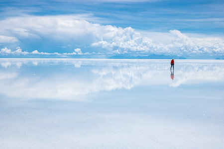 A person in the Uyuni Desert with the reflections of white clouds in Boliviaの写真素材