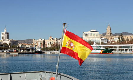 Malaga, Spain: Spanish flag waving in front of the skyline of the old town and the central harbour on a bright winters dayの写真素材