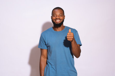 A young Nigerian man with a blue t-shirt smiling and showing like gesture on a white background.の写真素材