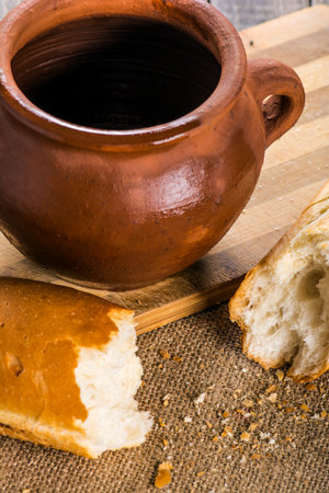 A closeup of an empty Clay pot and baguette on a wooden table